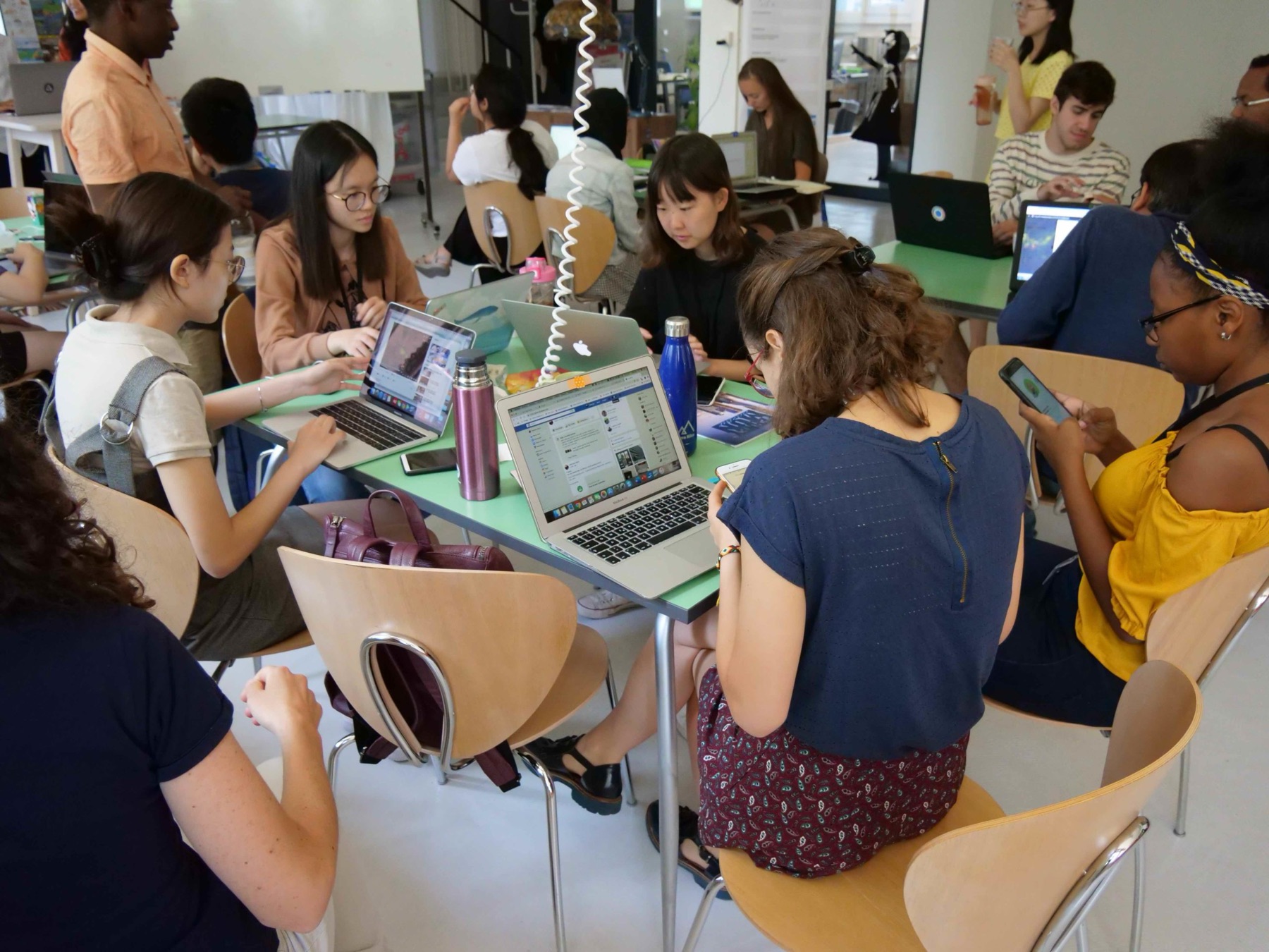 Summer school students working in teams on laptops around a table in the Solution Space